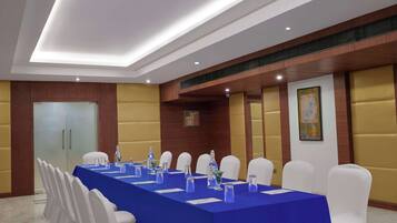 Un salón de conferencias con una mesa larga, sillas blancas y manteles azules.