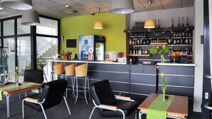 Un espace bar moderne, doté de sièges et d’un comptoir, avec un mur végétal, des luminaires suspendus et une variété de bouteilles et de verres.
