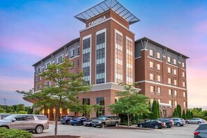 A multi-story hotel with a prominent 'CAMBRIA' sign, featuring a brick facade, large windows, and a covered entrance area.
