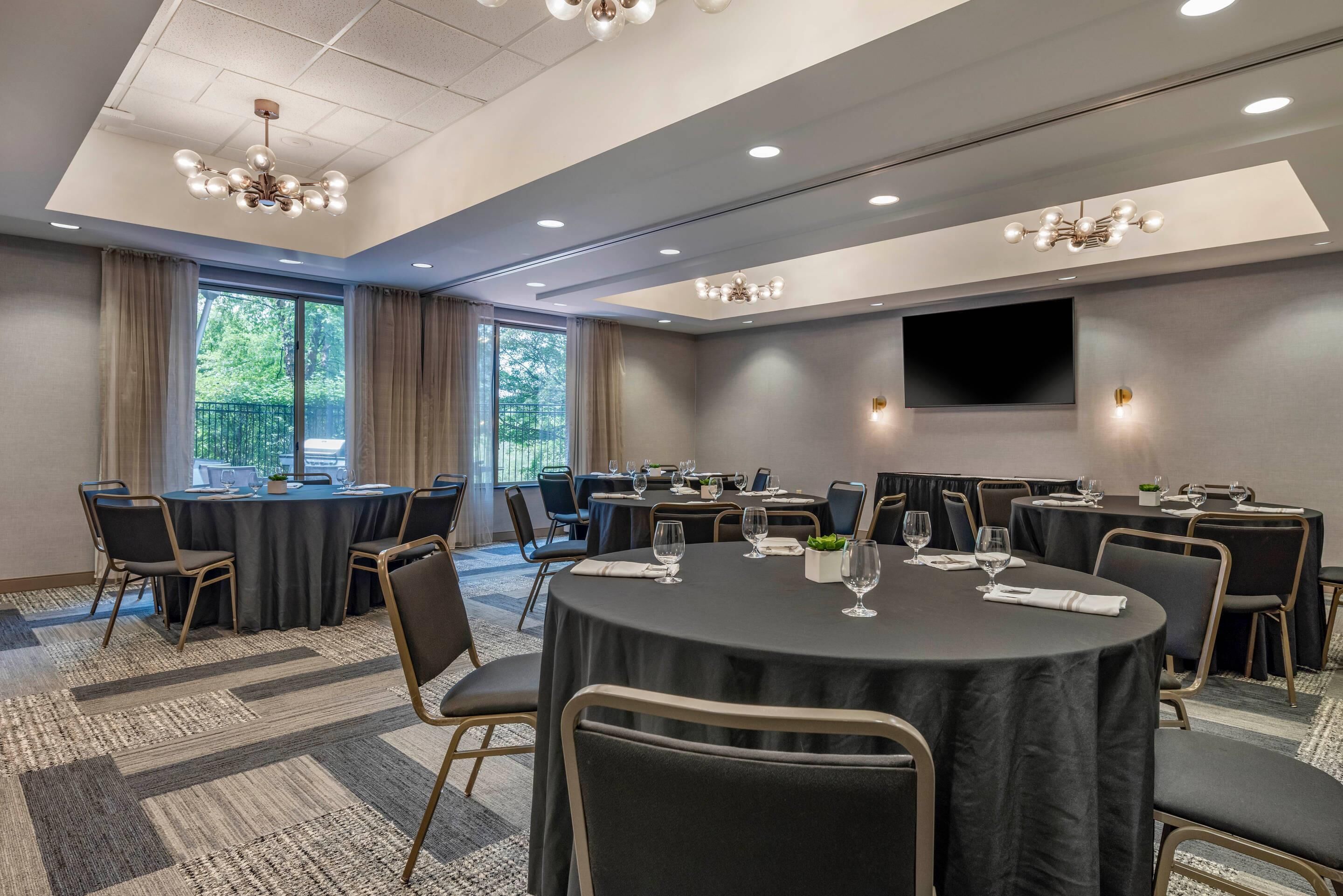 A conference room with round tables, chairs, and a large TV screen.