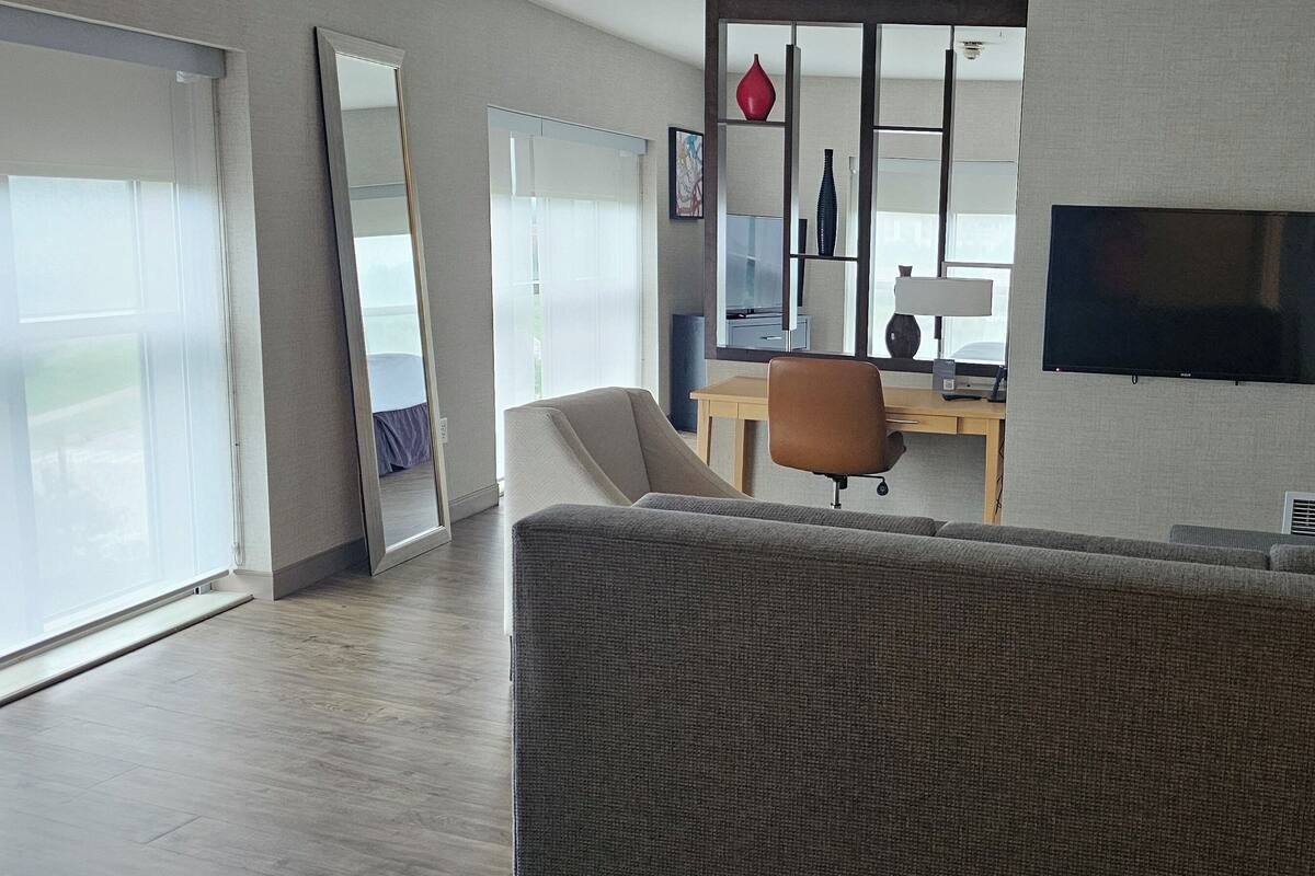 Una sala moderna con sofá, escritorio, televisor y un amplio ventanal.