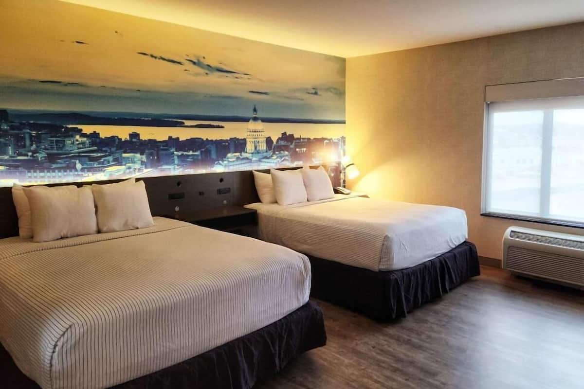 Habitación de hotel con dos camas, un mural de un paisaje urbano en la pared, una ventana y un calentador fijado a la pared.