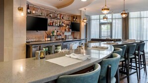 Uma área de bar moderna, com um balcão comprido, banquetas e uma televisão montada acima do balcão.