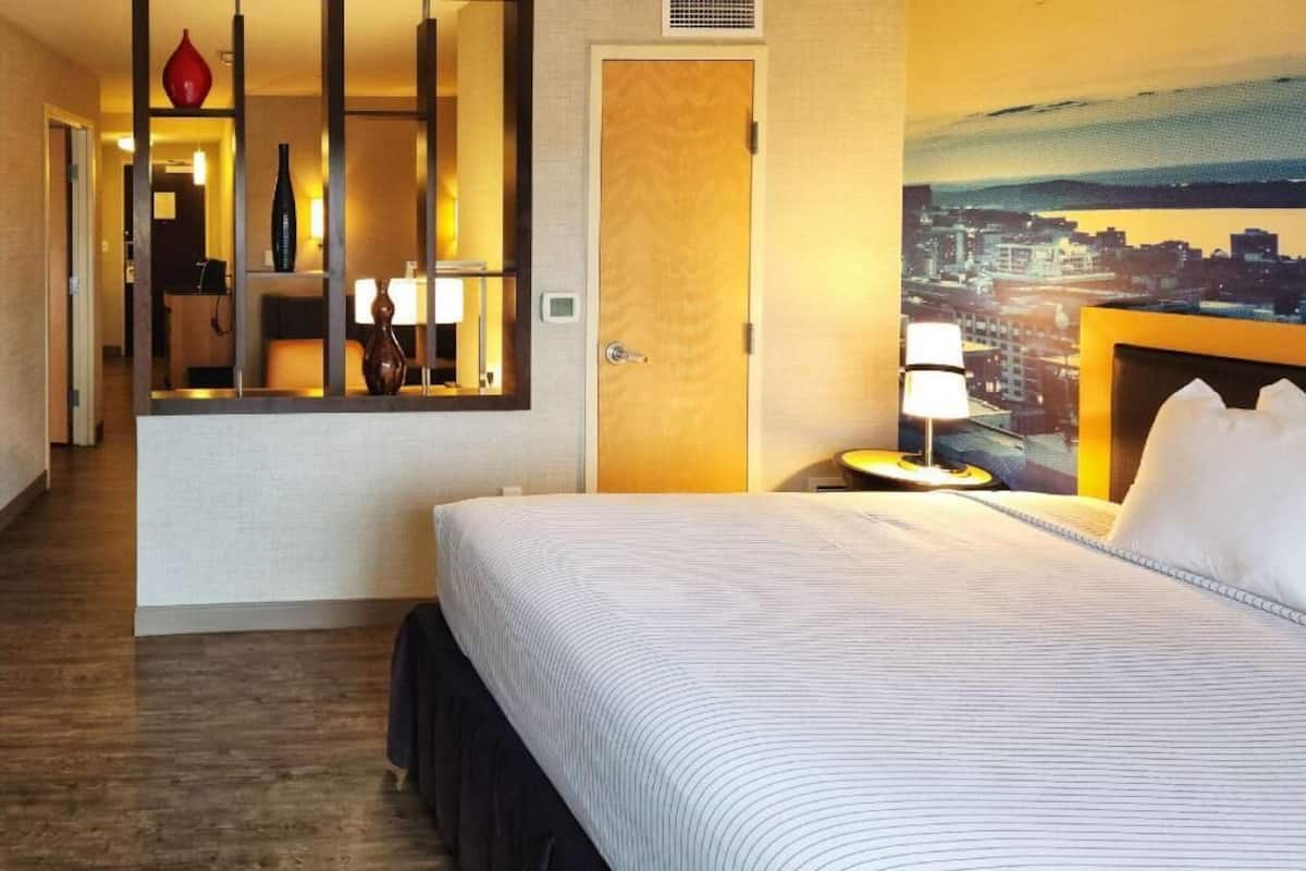 Una habitación de hotel con cama, mesita de noche, lámpara, espejo y puerta.