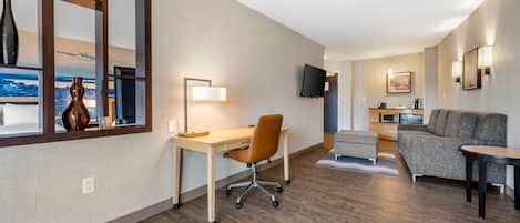 Una habitación de hotel moderna con un escritorio de madera, un sofá cómodo, un televisor de pantalla plana y vistas a la ciudad a través de un ventanal grande.