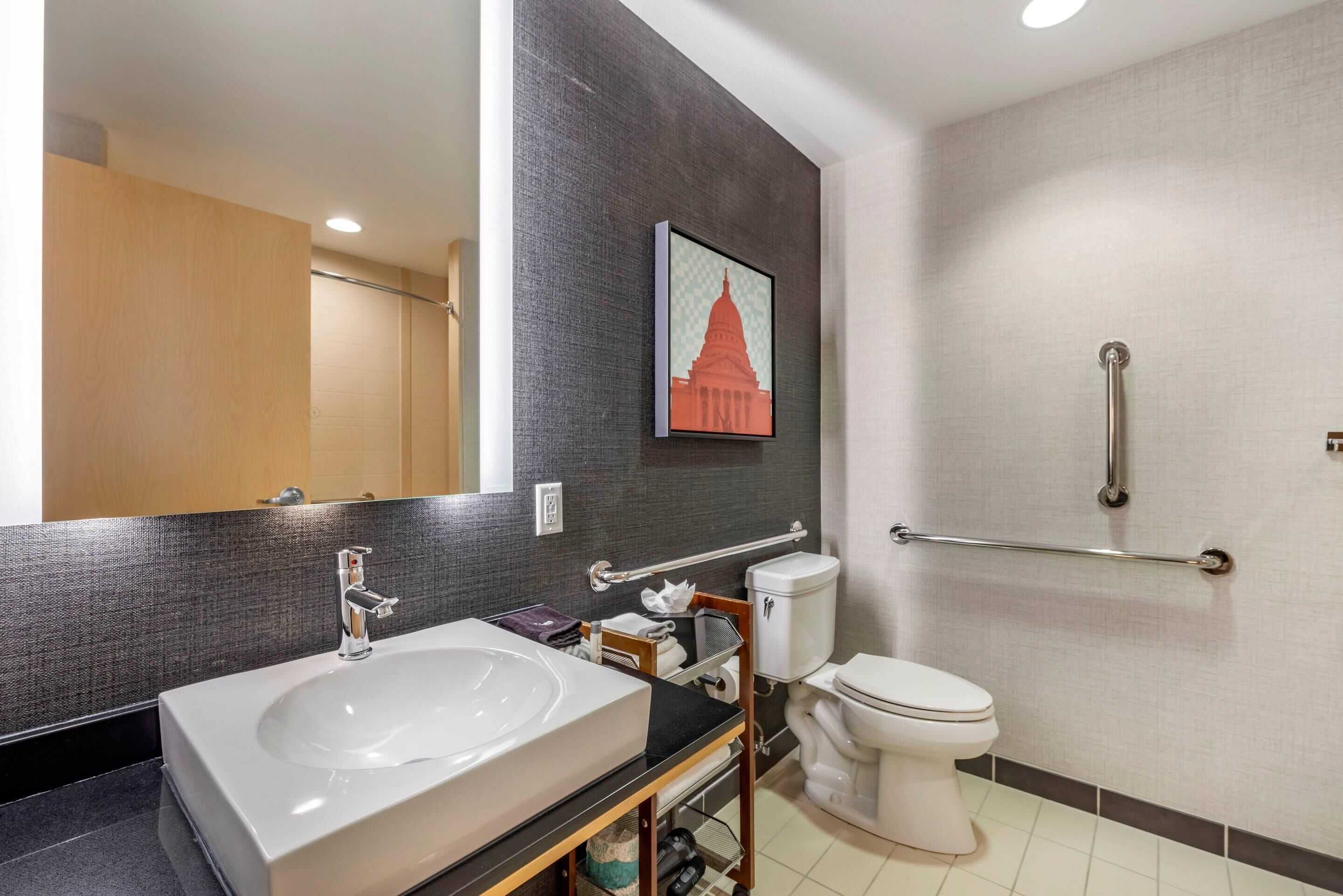 A modern bathroom with a large sink, toilet, and a shower area with grab bars.