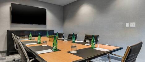 A conference room with a long table, chairs, a flat-screen TV, and water bottles.