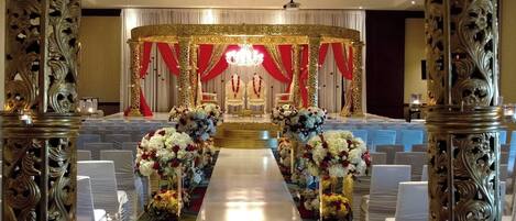 An ornate aisle with floral arrangements and a central stage with red drapes and a chandelier.