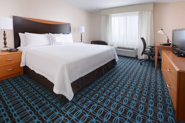 Habitación de hotel con una cama grande, un escritorio con computadora, una silla y un televisor.