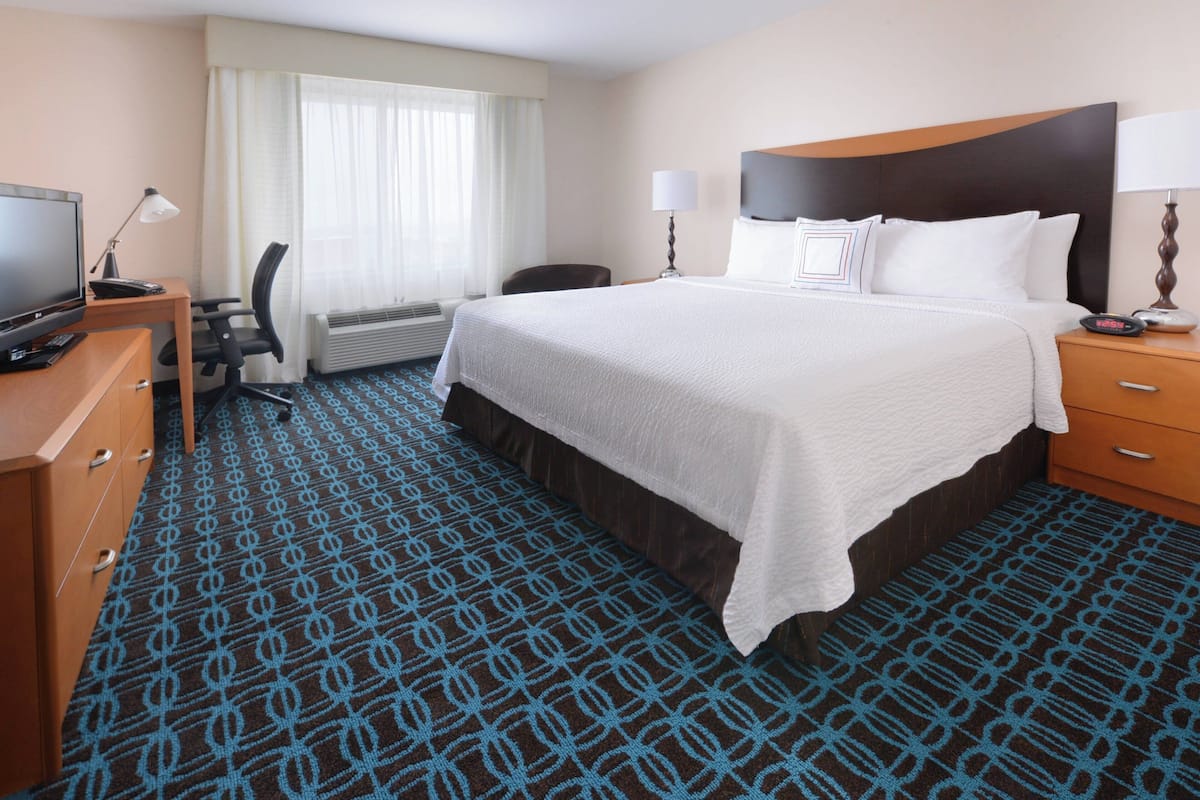 A hotel room with a large bed, a desk with a computer, a chair, and a TV.