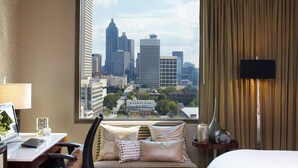 A hotel room with a cityscape view, a desk with a laptop, a sofa with patterned cushions, and a bedside table with a vase and a clock. - Renaissance Atlanta Midtown Hotel (Atlanta)