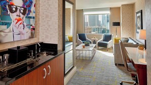 A modern hotel room with a kitchen area, a living room with a sofa and chairs, and a large window offering a city view. - Renaissance Atlanta Midtown Hotel (Atlanta)