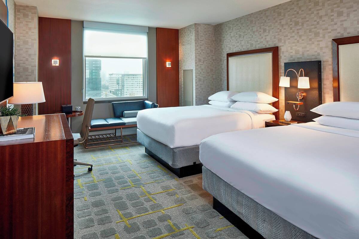 Ein Hotelzimmer mit zwei Betten, einem Schreibtisch, einem Stuhl, einem Fernseher und einem großen Fenster.