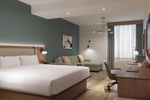 A modern hotel room with a large bed, a desk, a sofa, and a painting on the wall. - Hawthorn Extended Stay by Wyndham Kilgore (Kilgore)