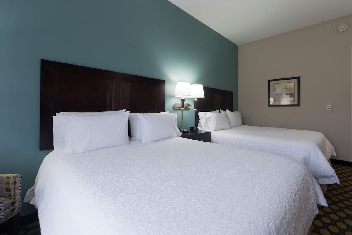 A hotel room with two beds, a nightstand with a lamp, and a framed picture on the wall.