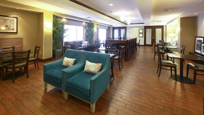A spacious lobby with a teal sofa, wooden chairs, a bar area, and a dining section. - Hampton Inn North Brunswick / New Brunswick (North Brunswick)