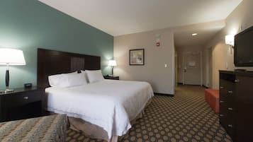 A hotel room with a large bed, bedside tables, a TV, and a patterned carpet.