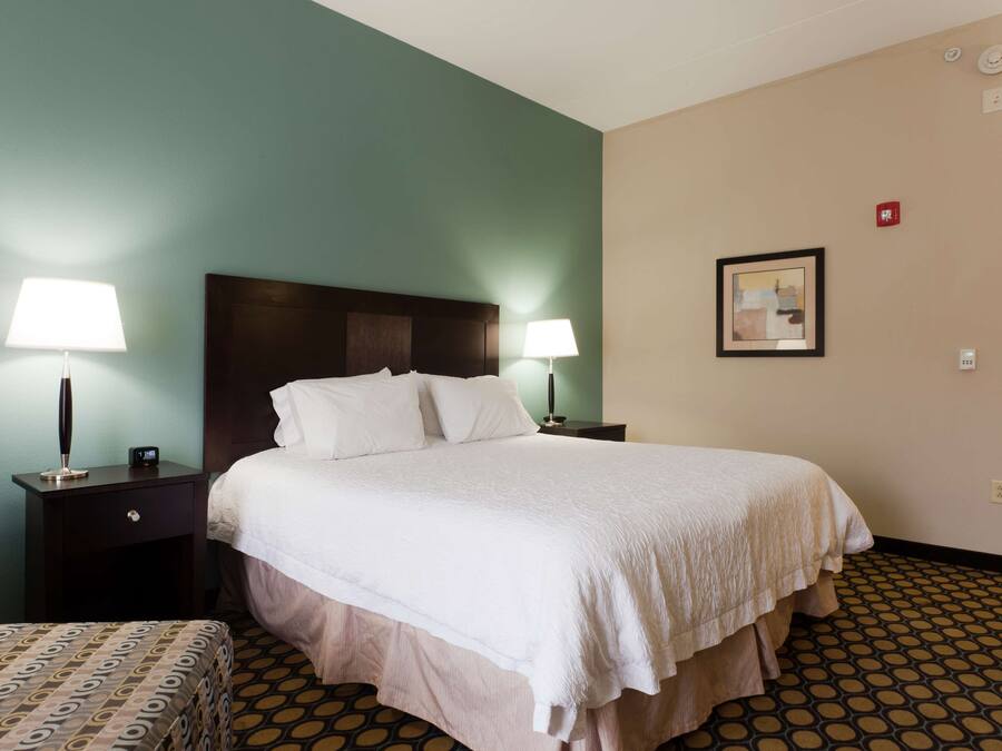 A hotel room with a large bed, two bedside tables with lamps, a headboard, a framed picture on the wall, and a patterned floor.
