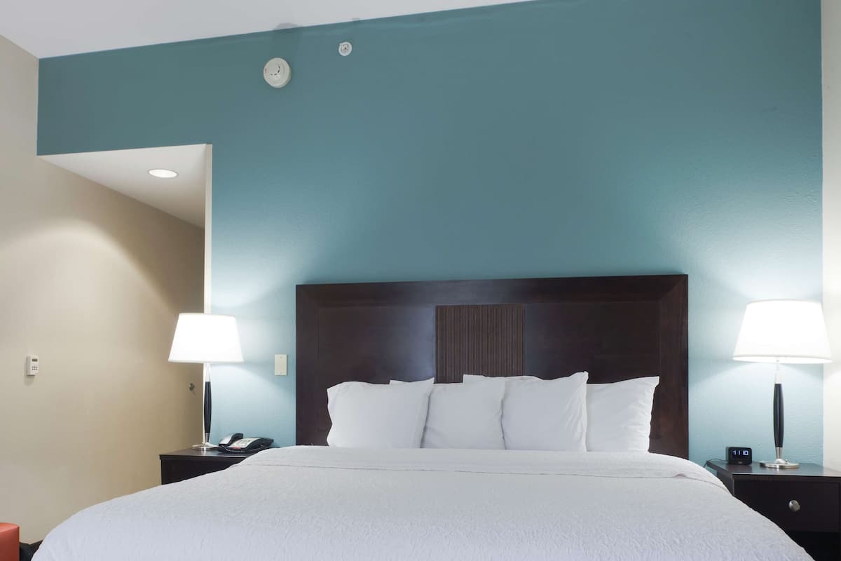 A hotel room with a large bed, two bedside tables with lamps, a wall clock, and a smoke detector.