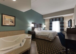 A hotel room with a large bed, a desk, a chair, a desk lamp, a TV, a bathroom with a bathtub, and a framed picture on the wall. - Hampton Inn North Brunswick / New Brunswick (North Brunswick)