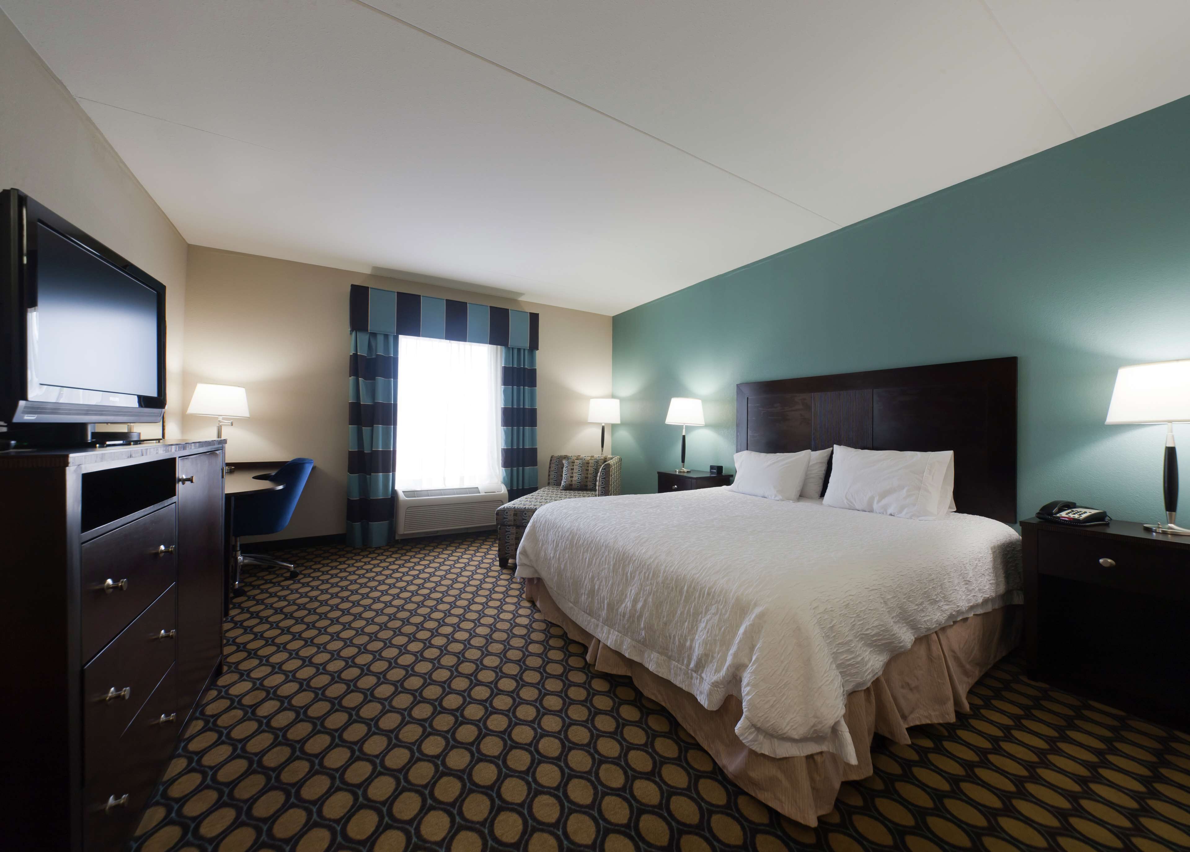 A hotel room with a large bed, a desk, a television, and a window with curtains.