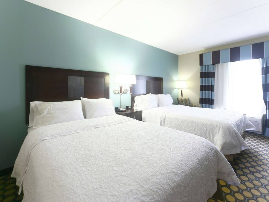 Ein Hotelzimmer mit zwei Betten, einem Nachttisch mit Lampe, einem Telefon und einem Fenster mit Vorhängen.