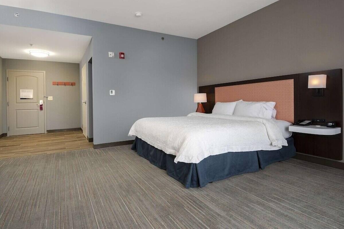A hotel room with a large bed, bedside lamps, a nightstand, and a door leading to another room.