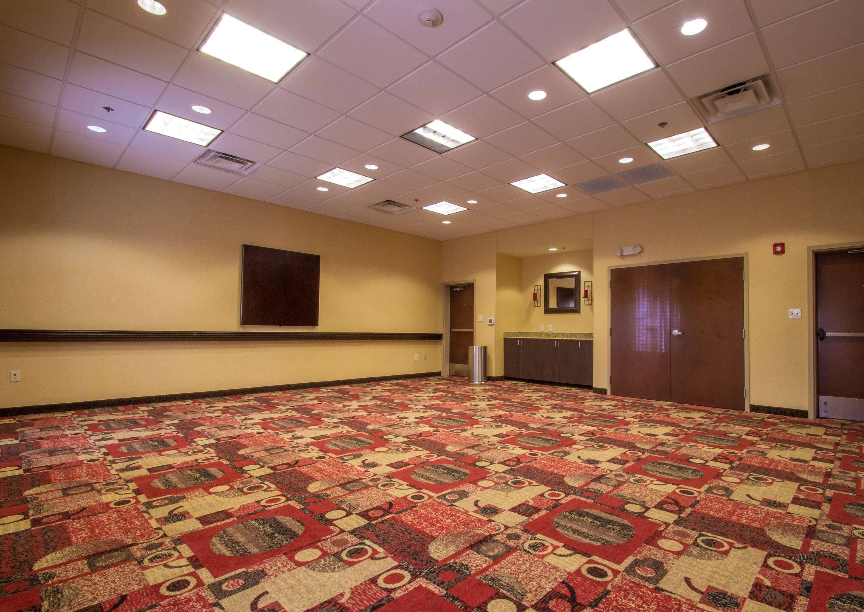 A conference room with a patterned carpet, recessed ceiling lights, a large mirror, and a kitchenette area.