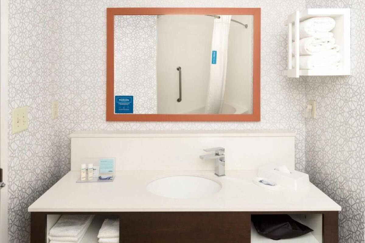 A bathroom with a sink, mirror, towel rack, and a cabinet with towels.