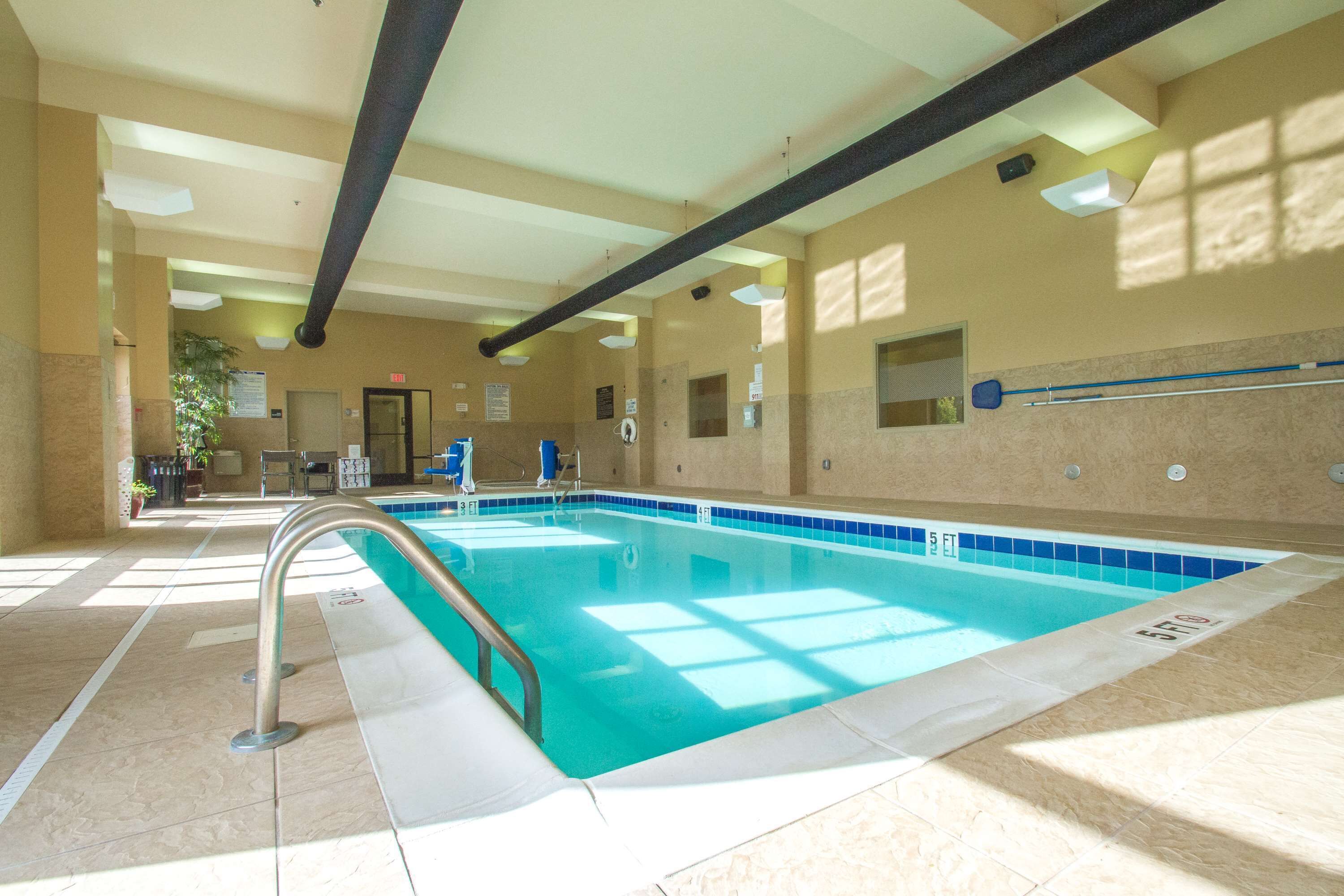 Uma piscina interior com água cristalina, uma escada de metal e paredes revestidas de azulejos.