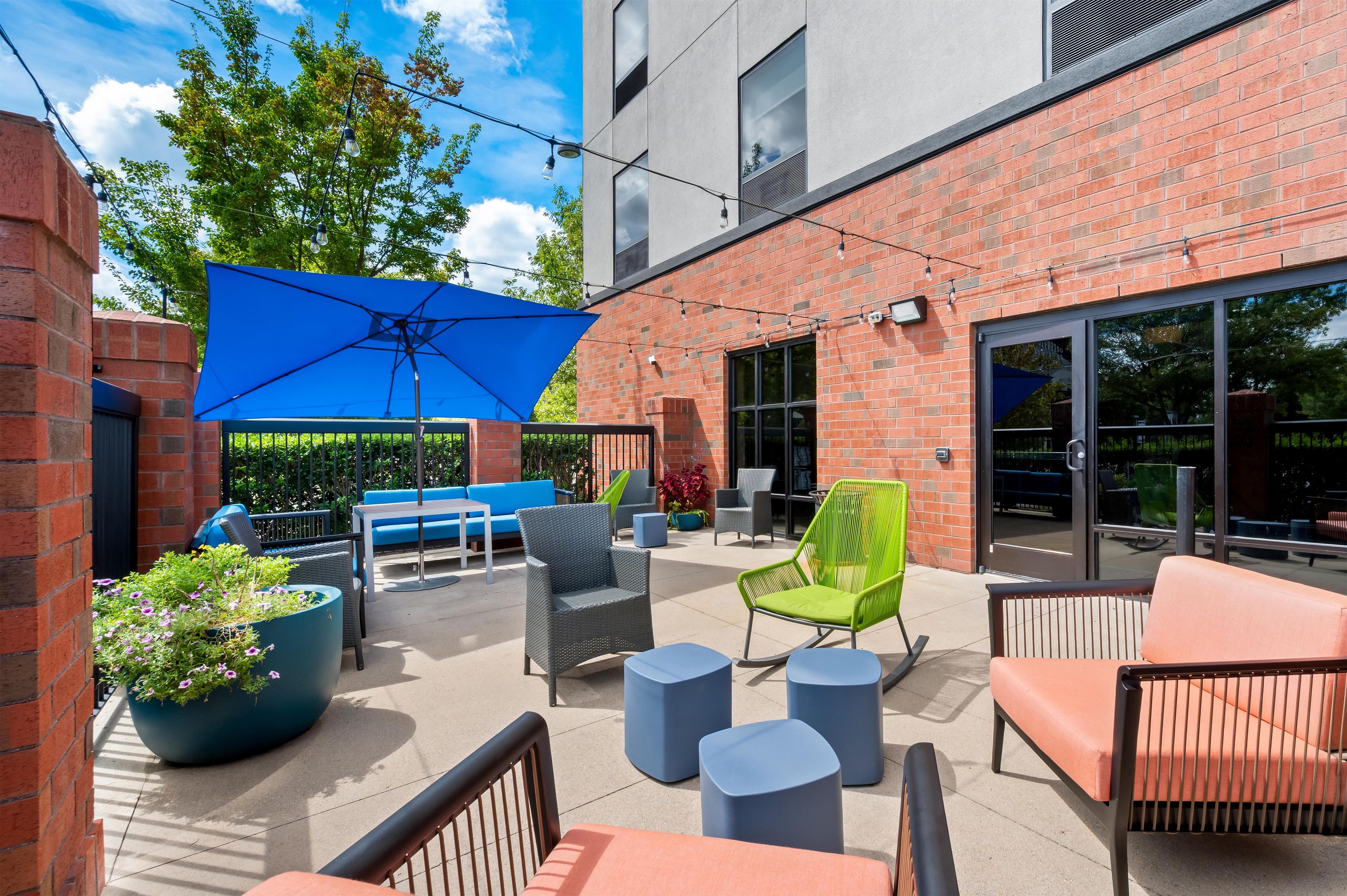 An outdoor patio with seating, a blue umbrella, and a brick building in the background.
