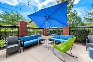 An outdoor patio with a blue umbrella, wicker furniture, and a brick wall. - Hampton Inn Greenville (Greenville)