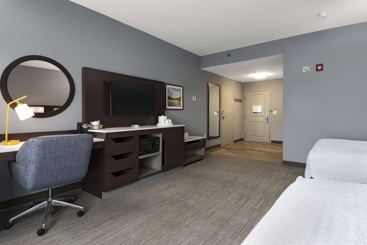 A hotel room with a desk, chair, bed, and a television.