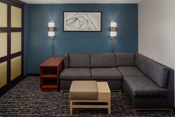 A modern living room with a gray sectional sofa, a wooden side table, a small ottoman, two floor lamps, and a geometric abstract painting on the wall. - Hyatt Place Uncasville - Casino Area (Montville)
