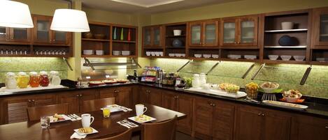 A well-lit kitchen with wooden cabinets, a breakfast bar, and various breakfast items displayed.