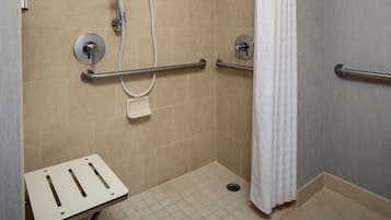 Un área de ducha con barras de apoyo, un cabezal de ducha manual y un asiento de ducha blanco.