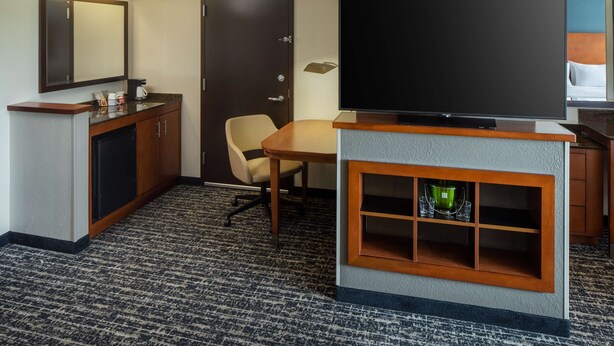 Habitación de hotel con televisión de pantalla plana, escritorio, silla, minibar y puerta.