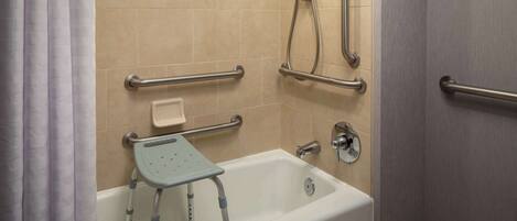 Un baño con bañera, barras de apoyo, cabezal de ducha y un accesorio de ducha de mano.