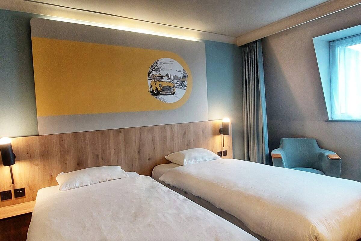 A hotel room with two beds, a wall-mounted artwork, a window with curtains, and a chair.