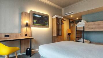 Una habitación de hotel con cama, escritorio, silla, televisor y literas.