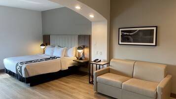 Quarto de hotel com uma cama, um sofá, uma escrivaninha com telefone e um quadro na parede.
