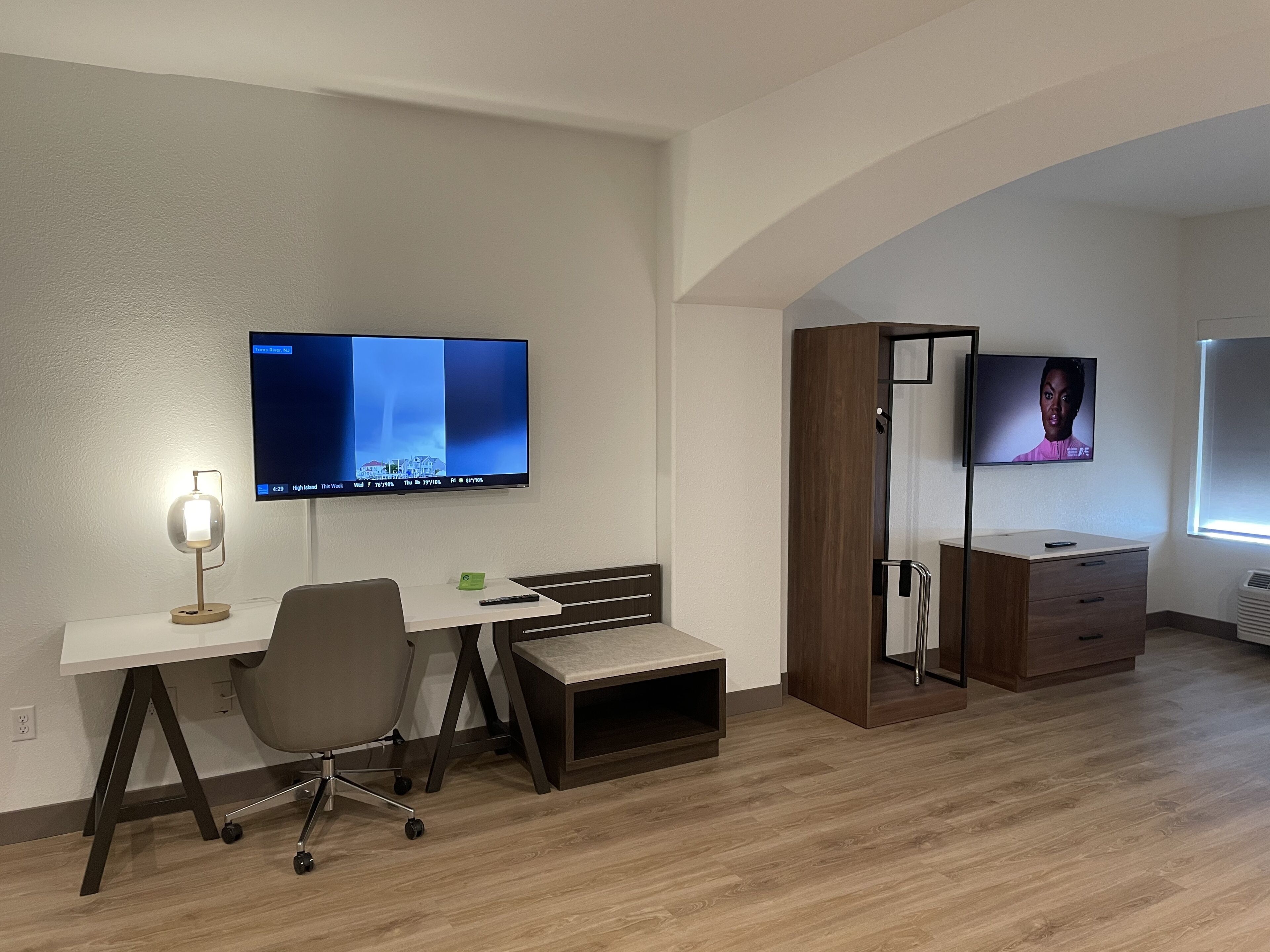 A modern hotel room with a desk, chair, and a TV mounted on the wall.