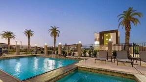 A swimming pool with a tiled edge, surrounded by palm trees and a fence. - La Quinta Inn & Suites by Wyndham Port Arthur (Port Arthur)