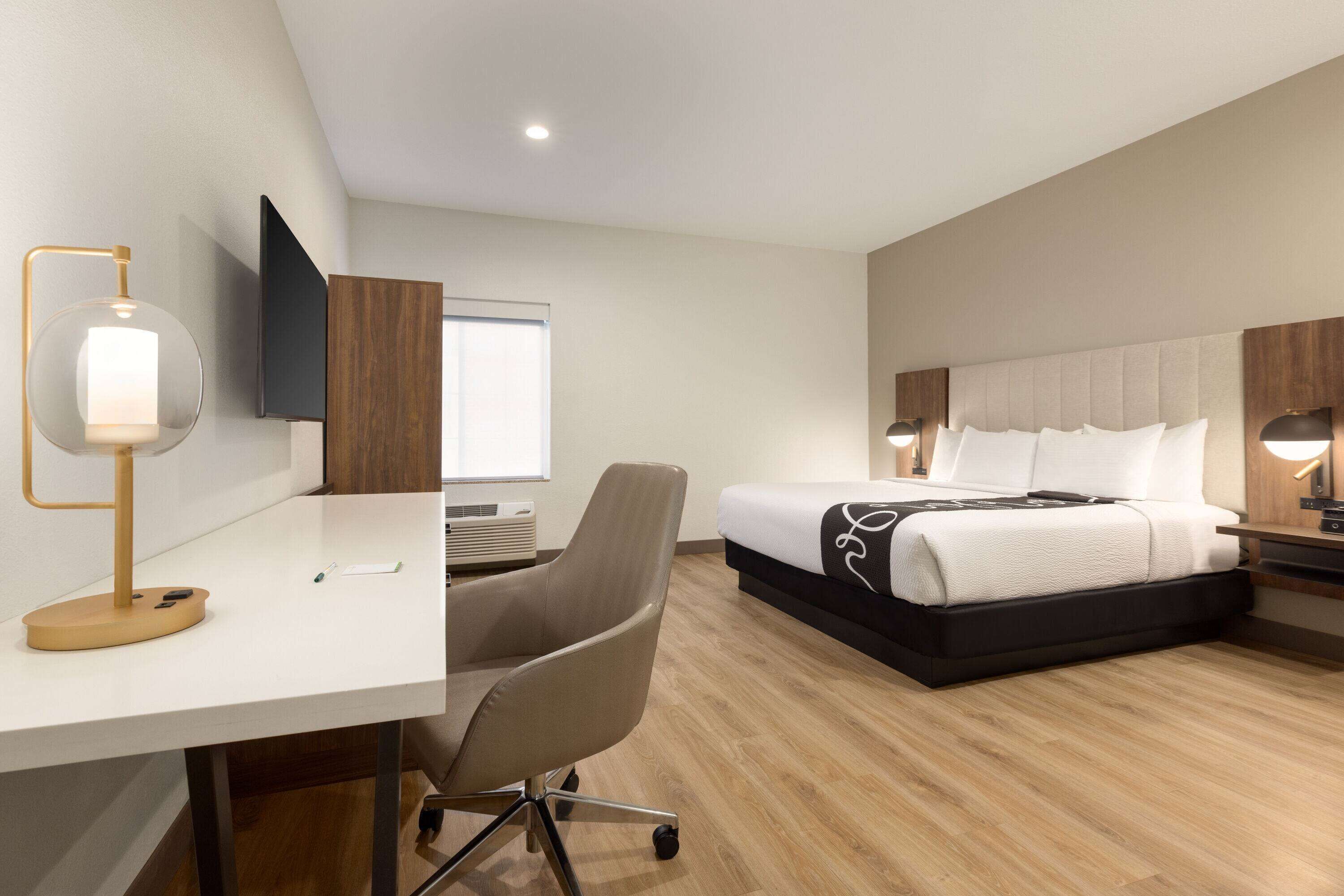 A hotel room with a desk, chair, bed, and a TV mounted on the wall.