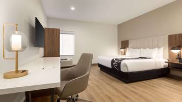 A hotel room with a desk, chair, bed, and a TV mounted on the wall.