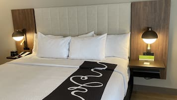 Una cama bien hecha con ropa blanca y un plaid blanco y negro. Hay dos mesitas de noche con lámparas, un teléfono y una tarjeta pequeña en una de ellas.