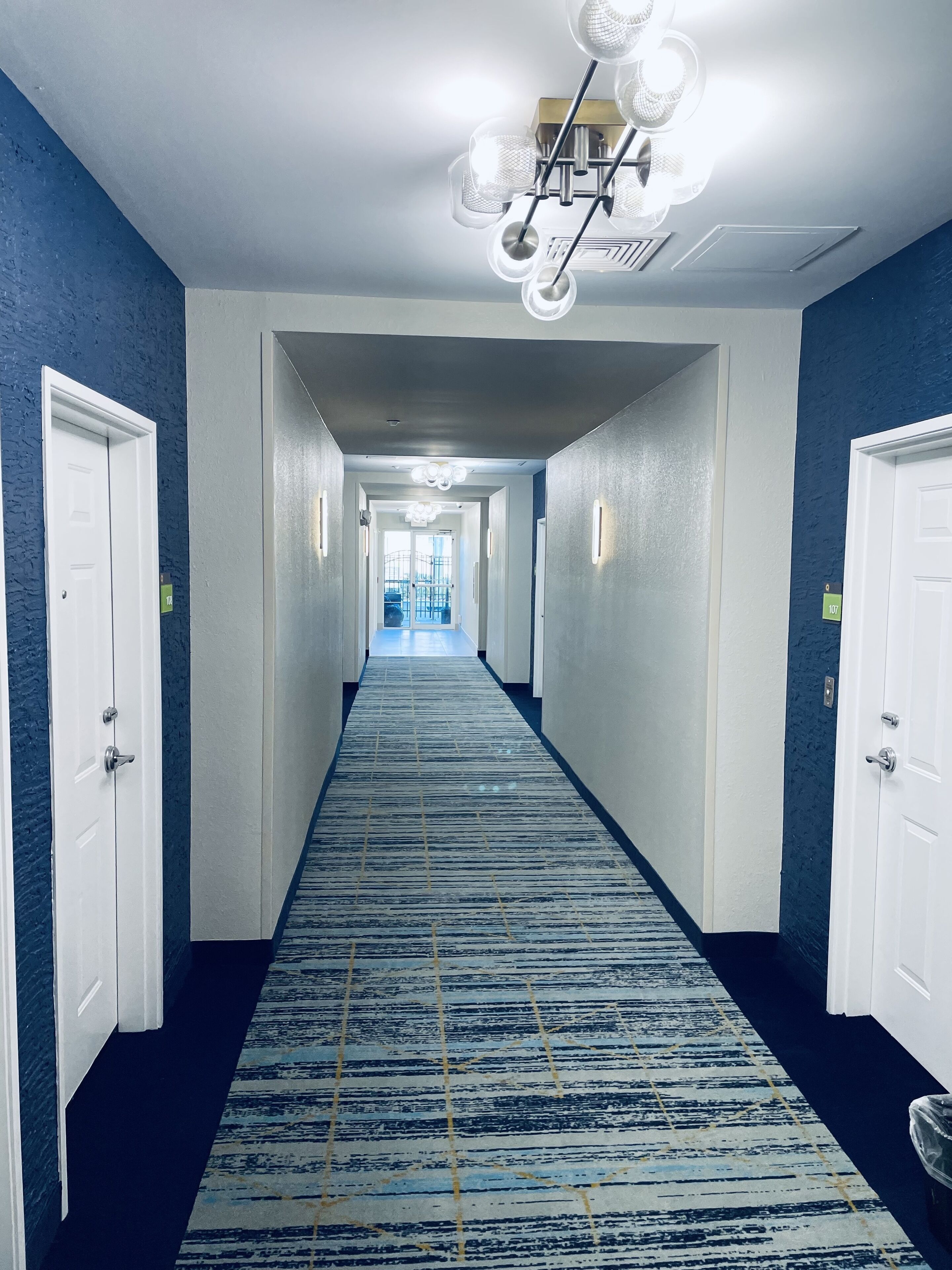 A hotel corridor with a blue carpet, white doors, and a chandelier.