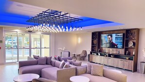 A modern living room with a sectional sofa, a TV, and a bar area. - La Quinta Inn & Suites by Wyndham Port Arthur (Port Arthur)