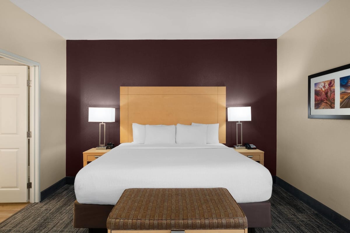 Habitación de hotel con una cama grande, dos lámparas de noche, un cabecero de madera, una mesita de noche y un cuadro en la pared.