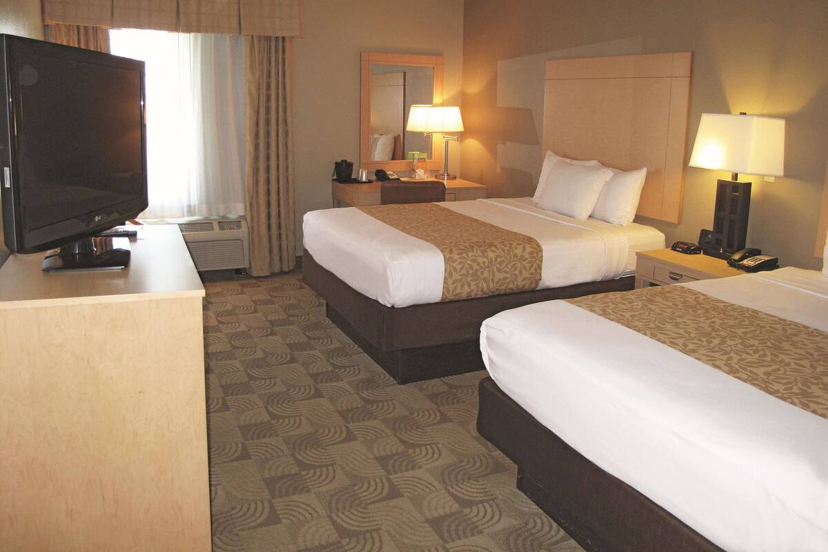 Habitación de hotel con dos camas, televisor, escritorio, lámpara y espejo.